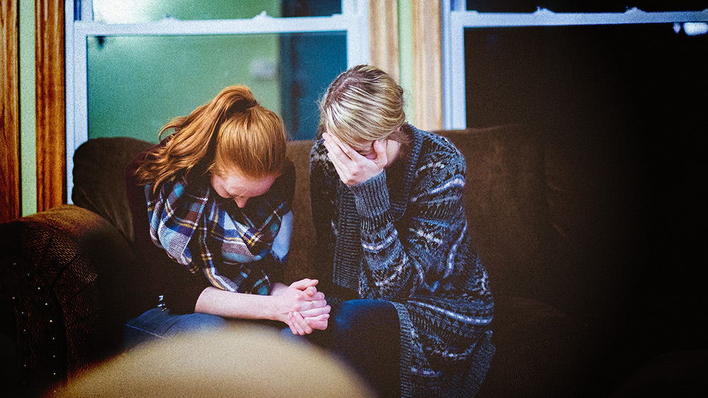 two women on couch praying